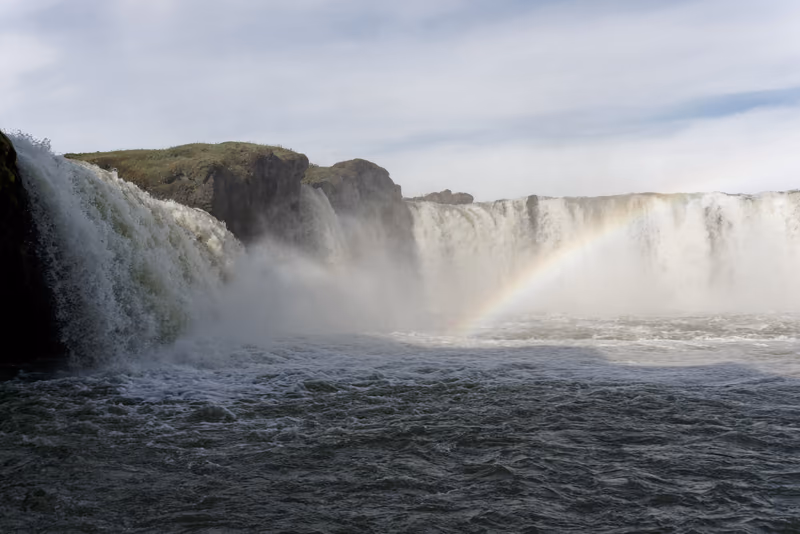 Goðafoss waterfall in a wide curtain, a rainbow rising from its spray