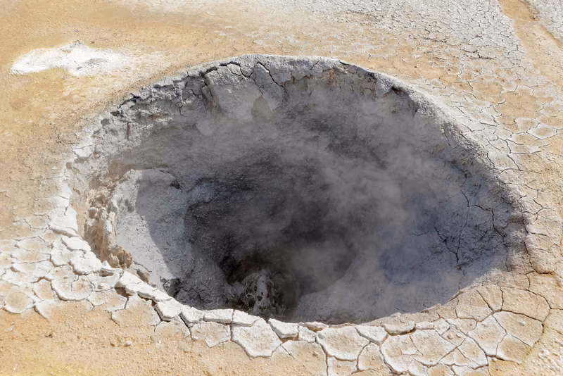 A grey mud pot steaming in the cracked clay of the Hverir geothermal field