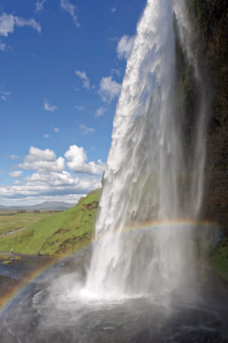 Seljalandsfoss seen from behind the falling water, a rainbow at its foot