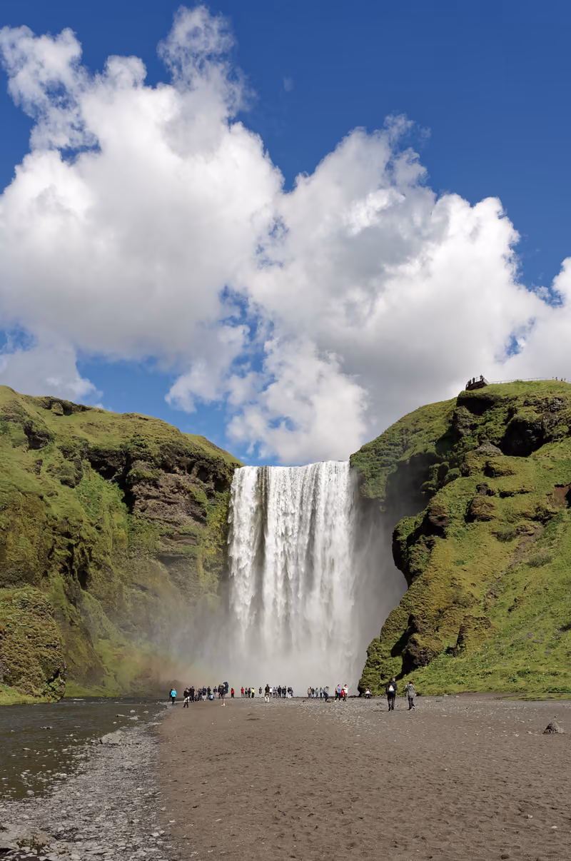 Skógafoss waterfall dropping from a green cliff under white clouds
